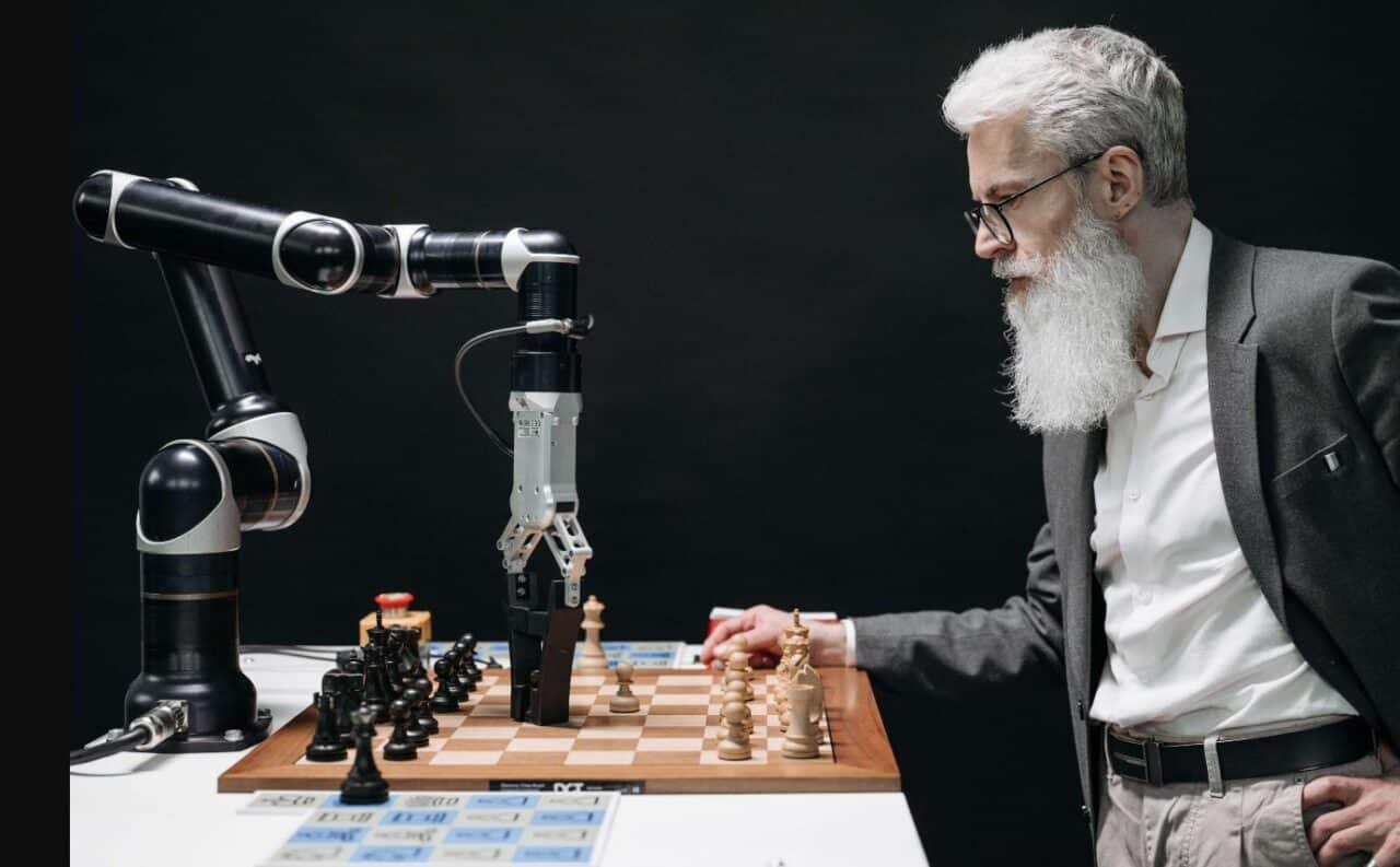 A bearded man with glasses engages in a game of chess with a robot, showcasing human-machine interaction