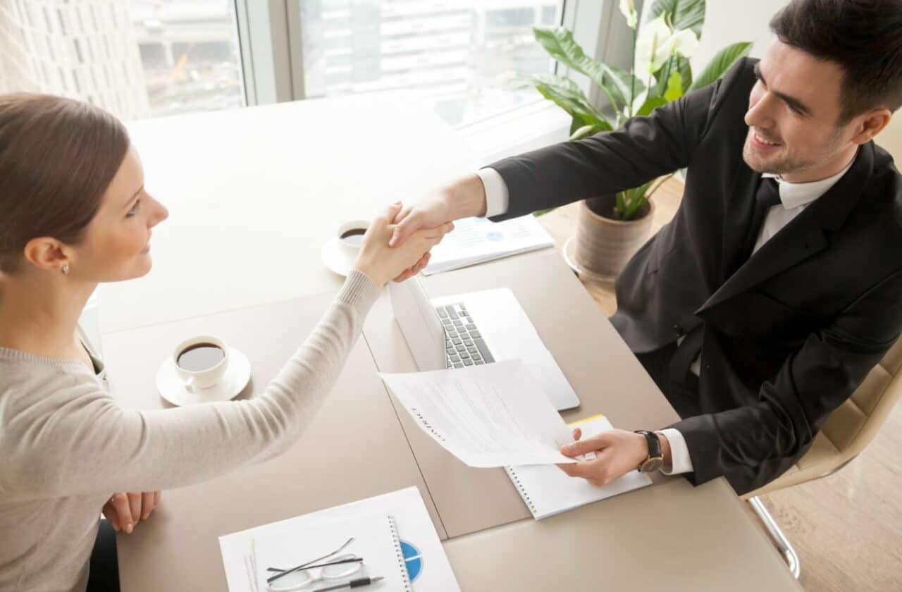 A professional man and woman shaking hands across a desk, symbolizing a formal agreement or partnership.
