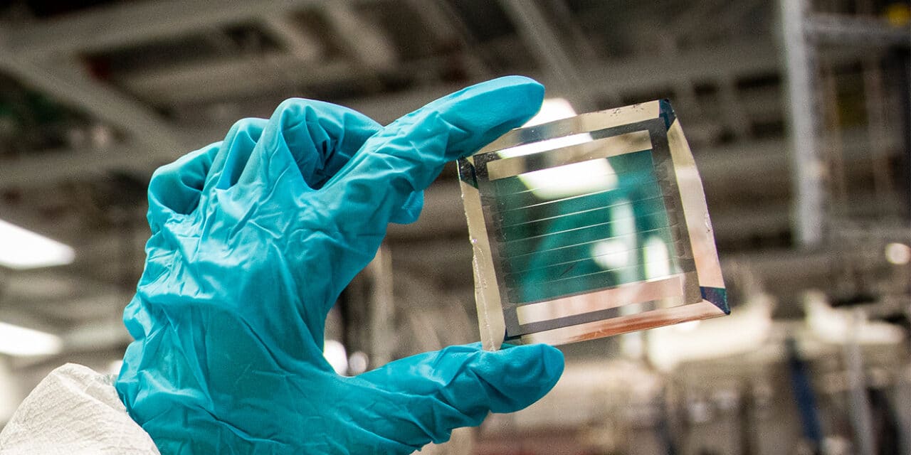 Person with blue gloves showcasing a small glass piece for a solar cell