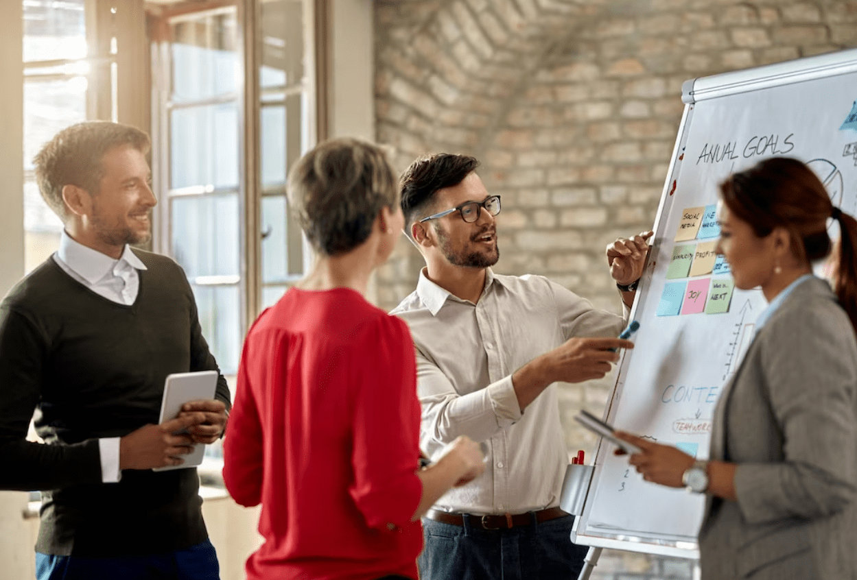 A group of professionals discussing ideas and strategies while standing around a whiteboard in a business setting.